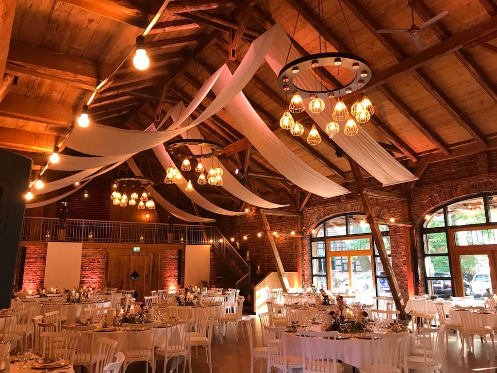 Hochzeitssaal mit Holzbalken, Lichterketten und Tuchdeko