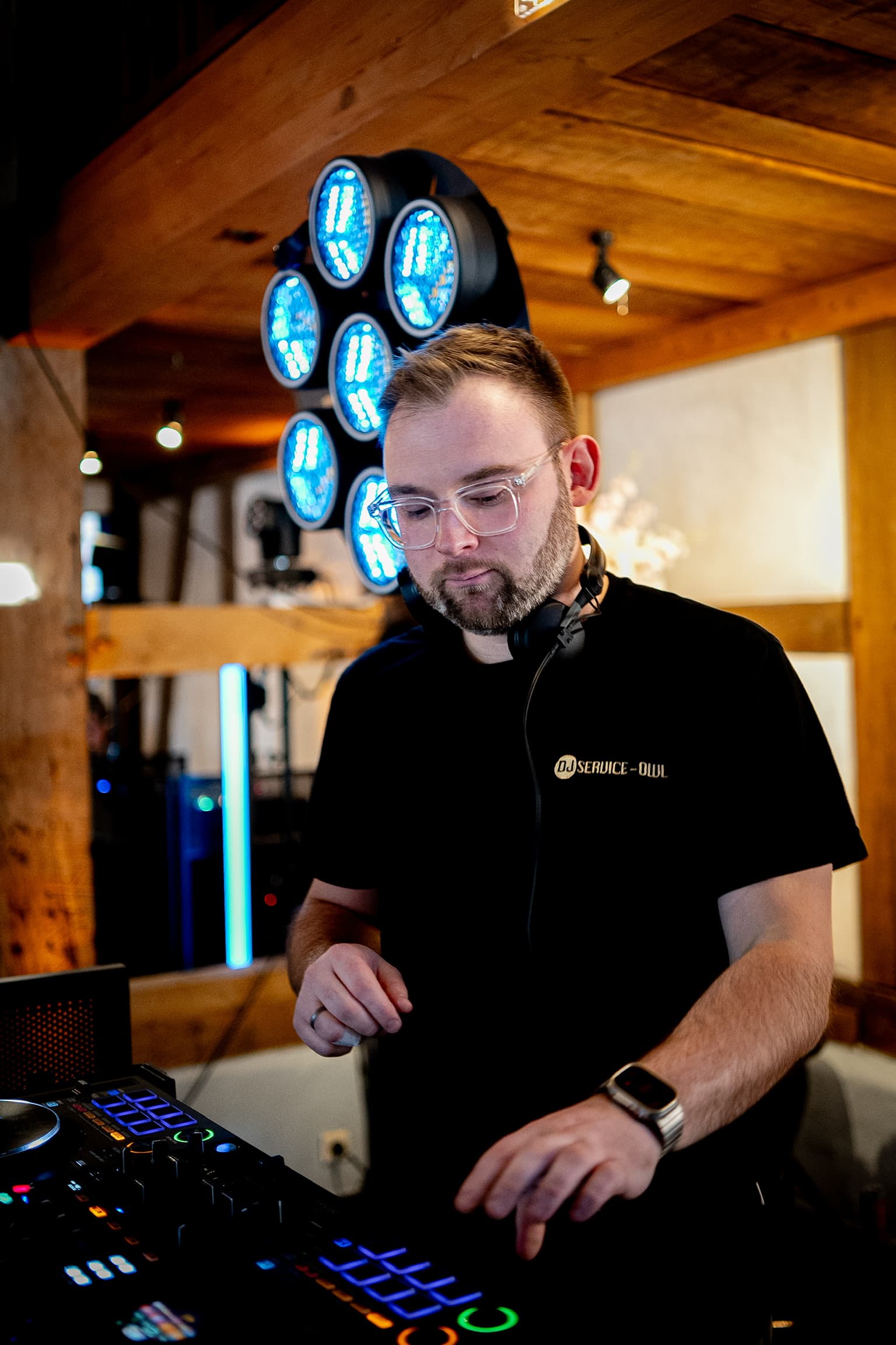 DJ Denis mit Kopfhörern am DJ-Pult vor einem leuchtenden Lichteffekt